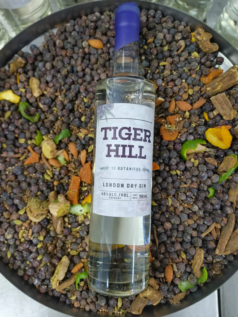 Bottle of Tiger Hill on a bed of botanicals: juniper berries, almonds, citrus peel and spices